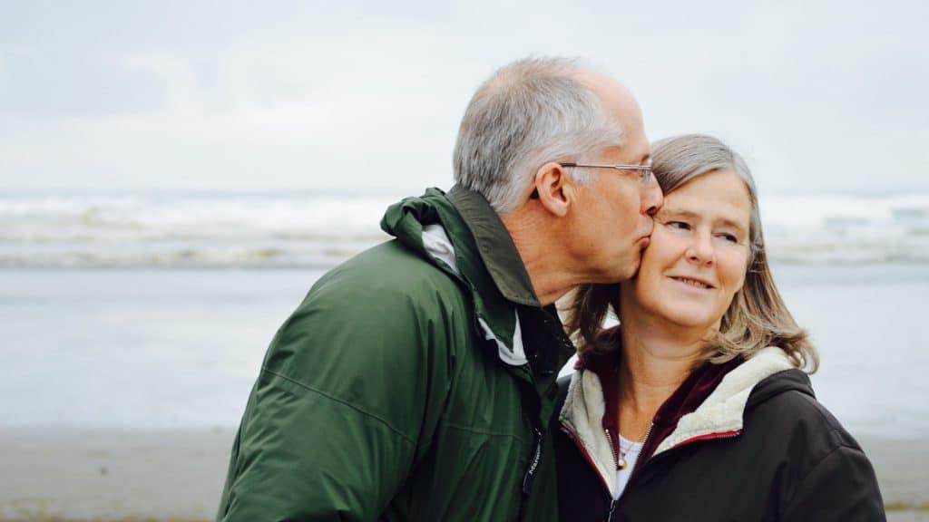 man kissing woman on check beside body of water