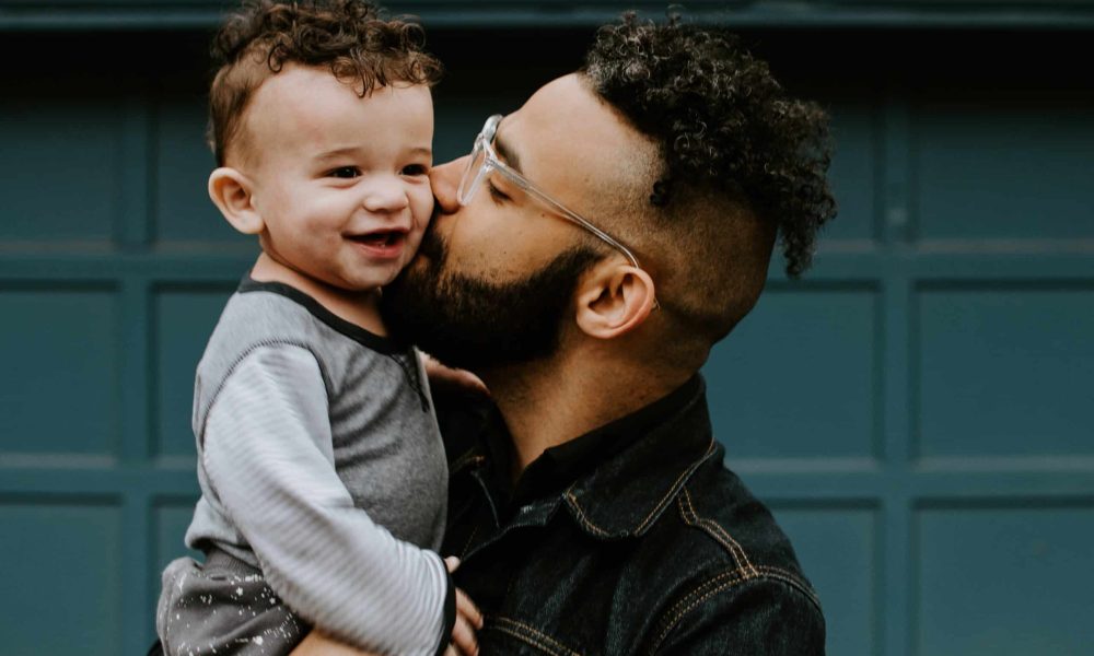 man carrying baby boy and kissing on cheek