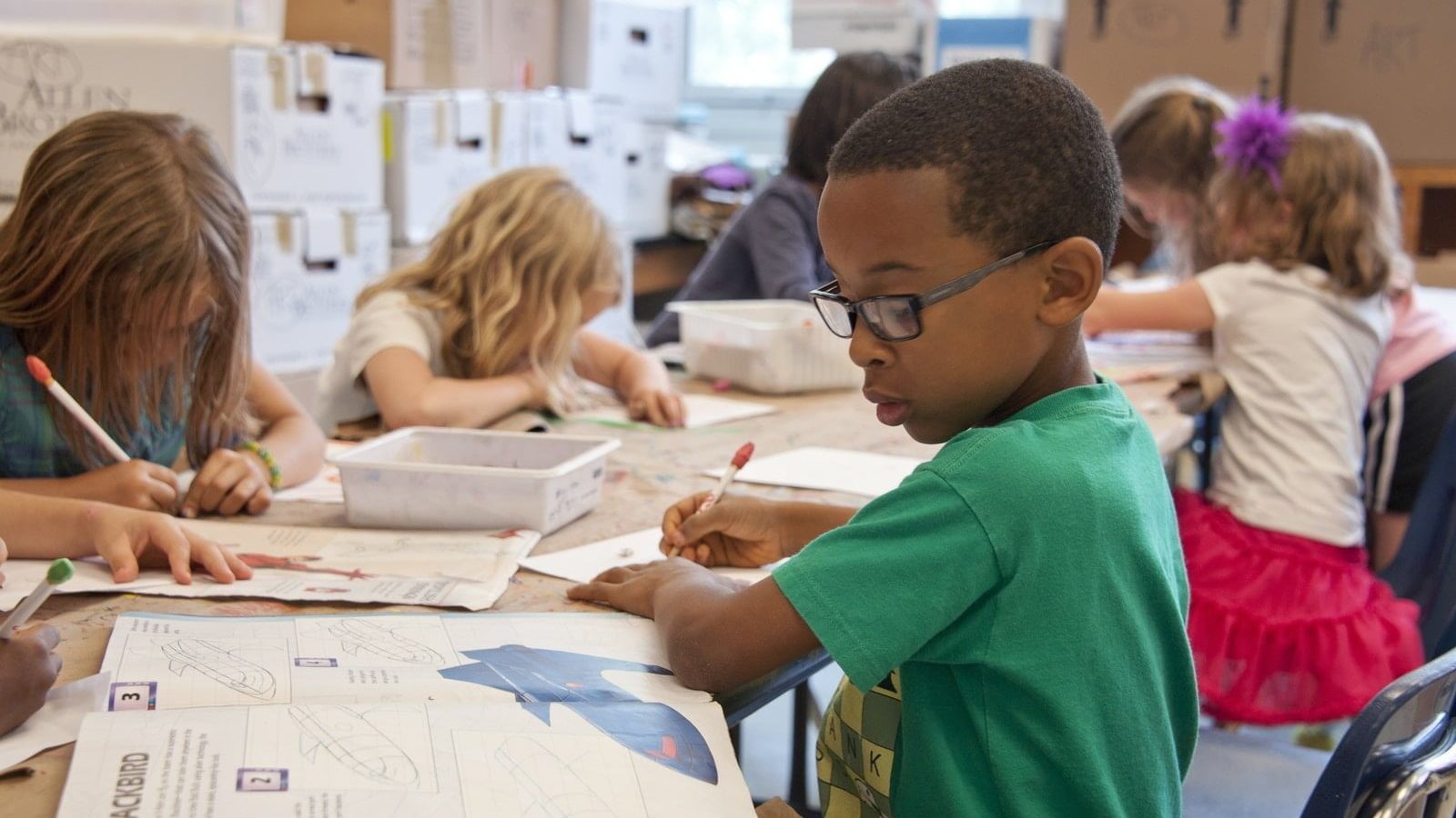 boy in green sweater writing on white paper